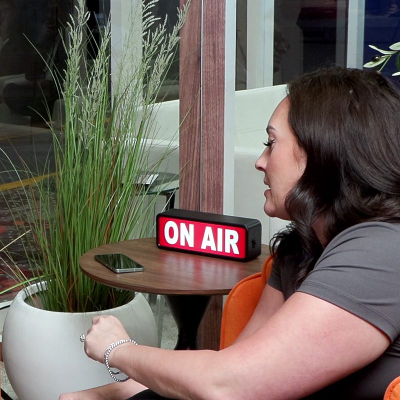 A guest talking on a podcast set, with an ON AIR sign on the table